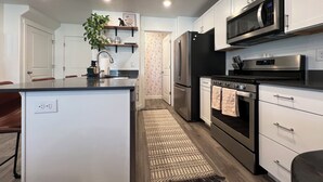 A modern kitchen with white cabinetry, stainless steel appliances, a central island, and a patterned rug.