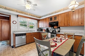 A kitchen with wooden cabinets, a dishwasher, a microwave, and a stove. There is a dining table with chairs and a red tablecloth.