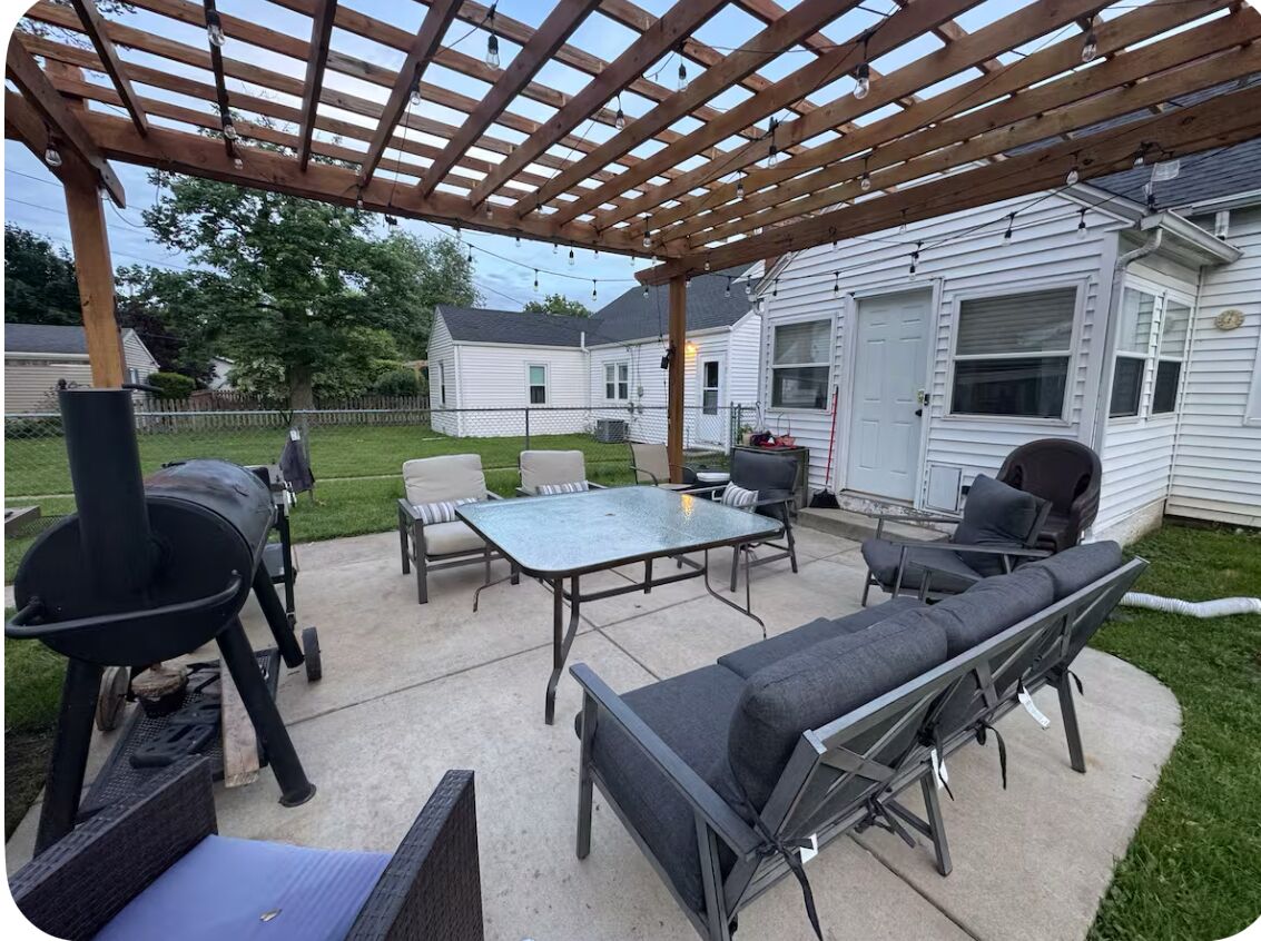Een terras buiten met een pergola, een barbecue, een tafel en zitplaatsen.