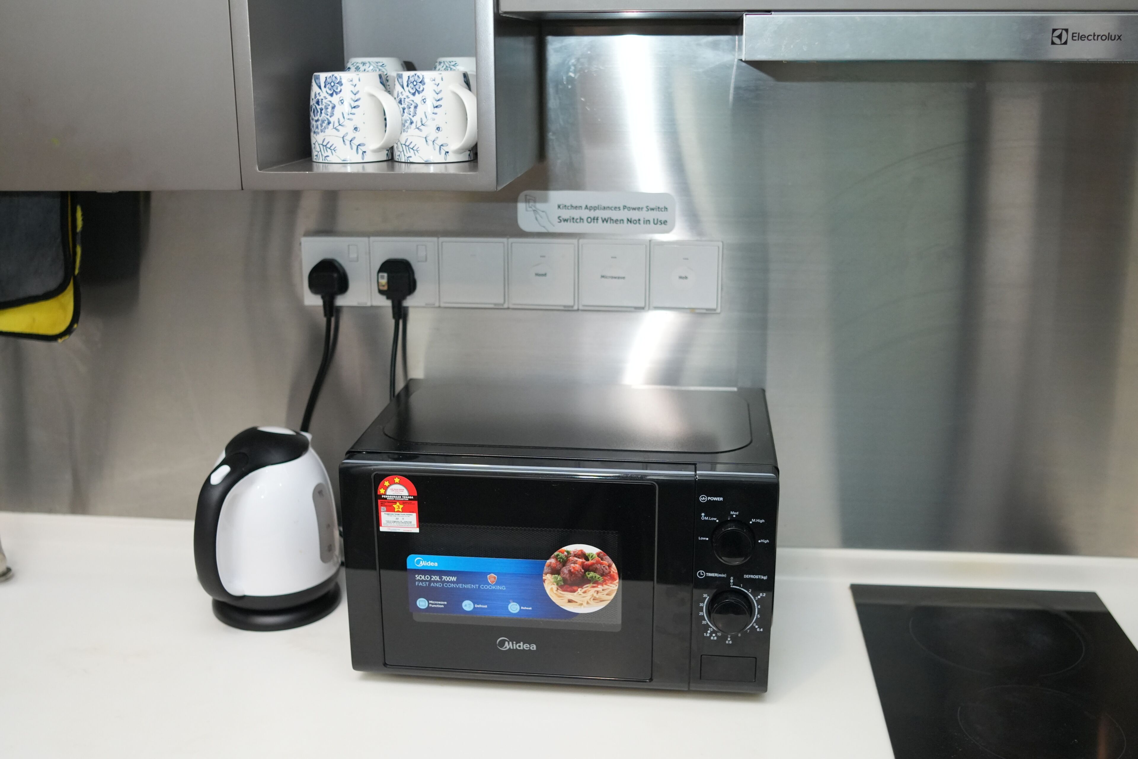 A kitchen with a microwave, a kettle, and a power switch.