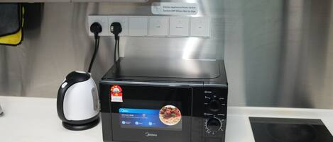 A kitchen with a microwave, a kettle, and a power switch.