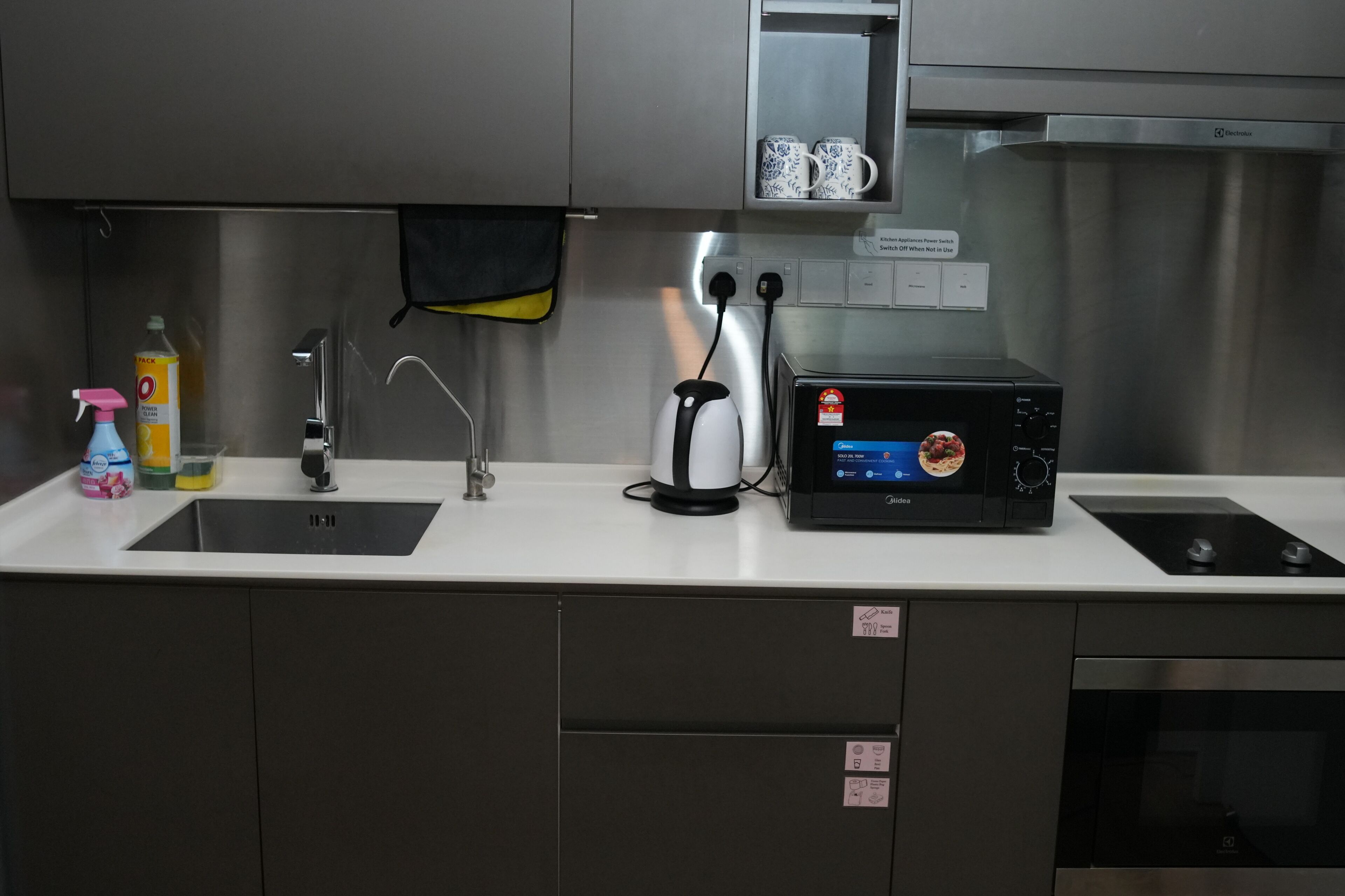 A kitchen with a microwave, toaster, sink, and stainless steel cabinets.