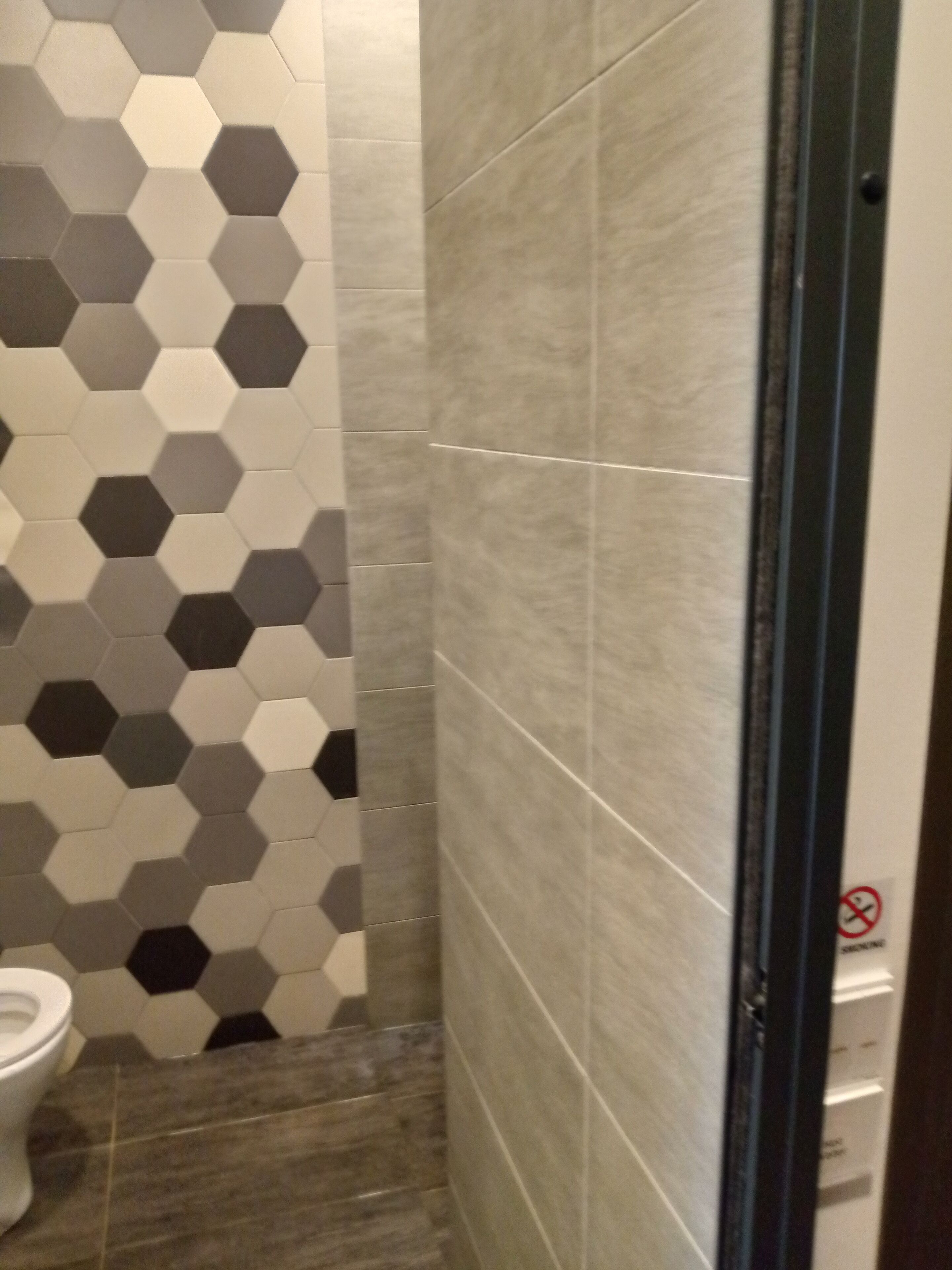 A bathroom with hexagonal patterned tiles on the wall, a toilet, and a shower area with large square tiles.