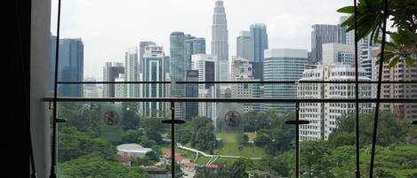 Vista desde una ventana con baranda de metal, sobre un paisaje urbano con rascacielos y un área verde.
