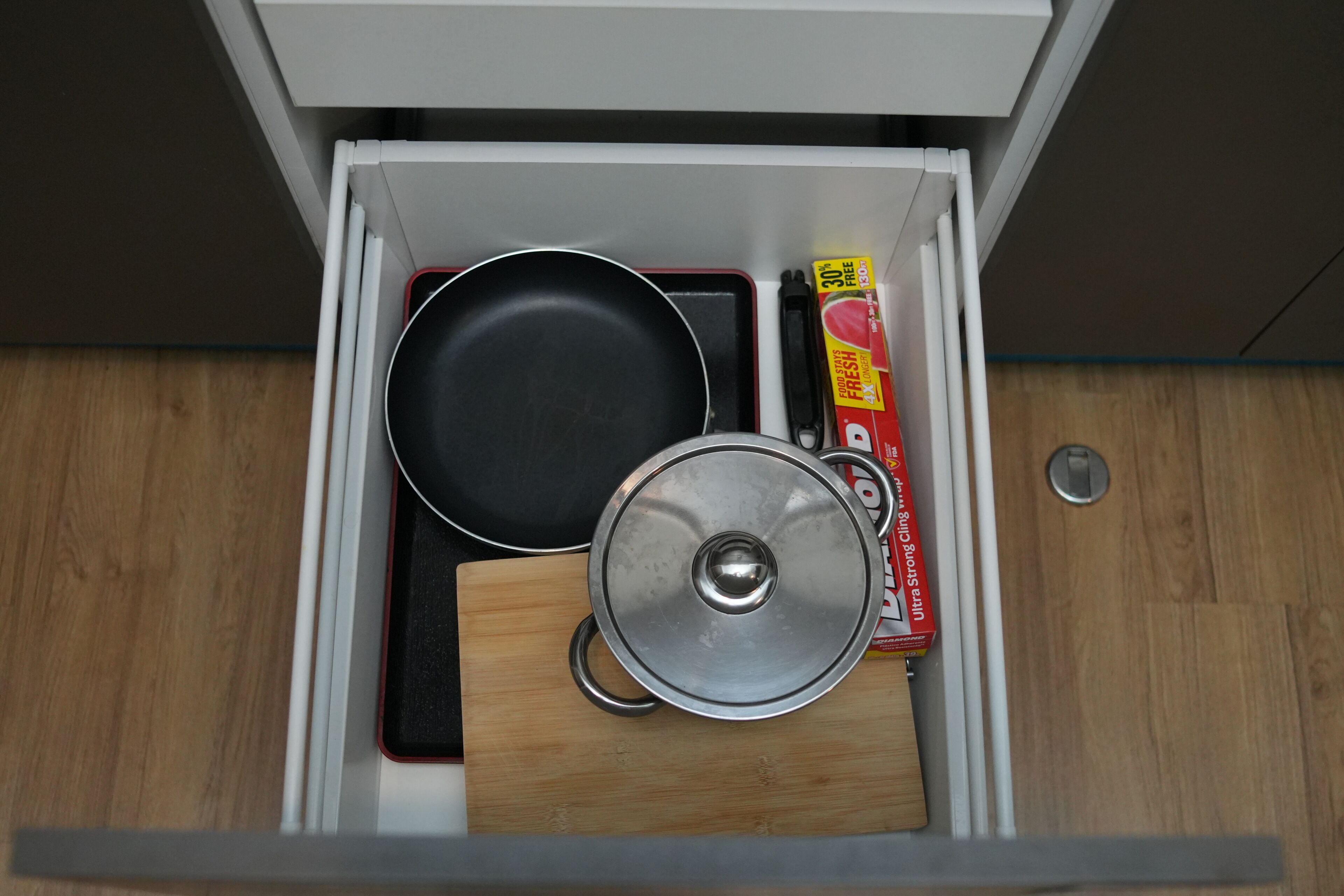 Een lade met een koekenpan, een pan en een doosje vershoudfolie.