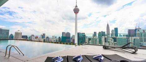 Zona de piscina en la azotea con sillones de descanso y vista al horizonte urbano, incluyendo una torre destacada.