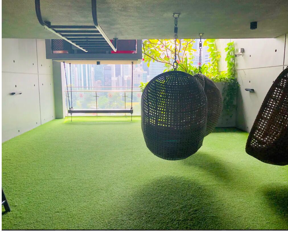 A room with green artificial turf, hanging exercise balls, and a large window with a city view.