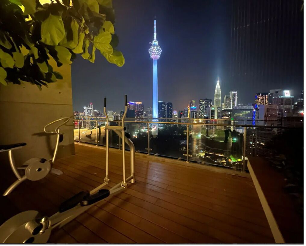 Un balcon équipé d’appareils de musculation, offrant une vue sur un paysage urbain avec des bâtiments illuminés et une tour imposante.