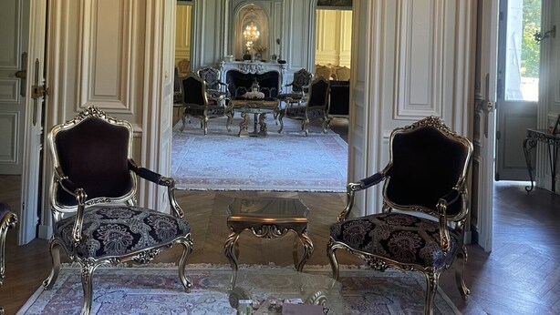 A grand room with ornate chandeliers, a fireplace, and classical furniture.