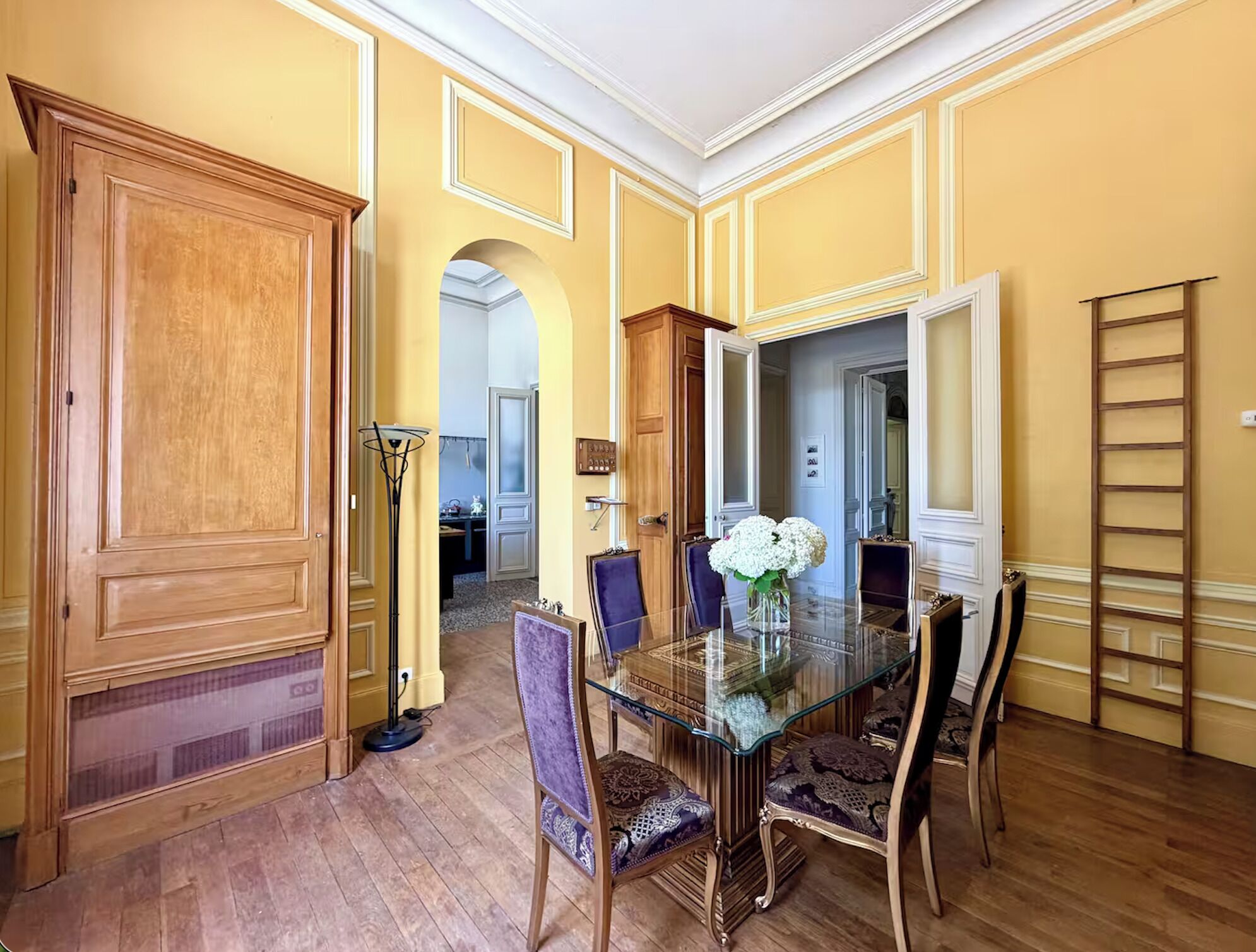 A dining room with a glass table, wooden chairs, and a large wooden cabinet.