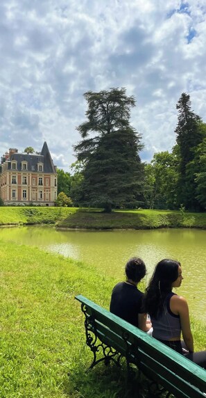 Un couple est assis sur un banc au bord d’un lac, avec un grand bâtiment en arrière-plan.