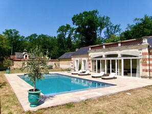 A swimming pool with lounge chairs, a covered patio, and a brick house with a tiled roof. - Chateau de La Briche & Private Pool House - Entire Loire Valley Estate (Hommes)
