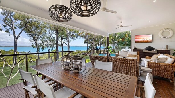 A wooden deck with a table and chairs, wicker furniture, a TV, and a grill.