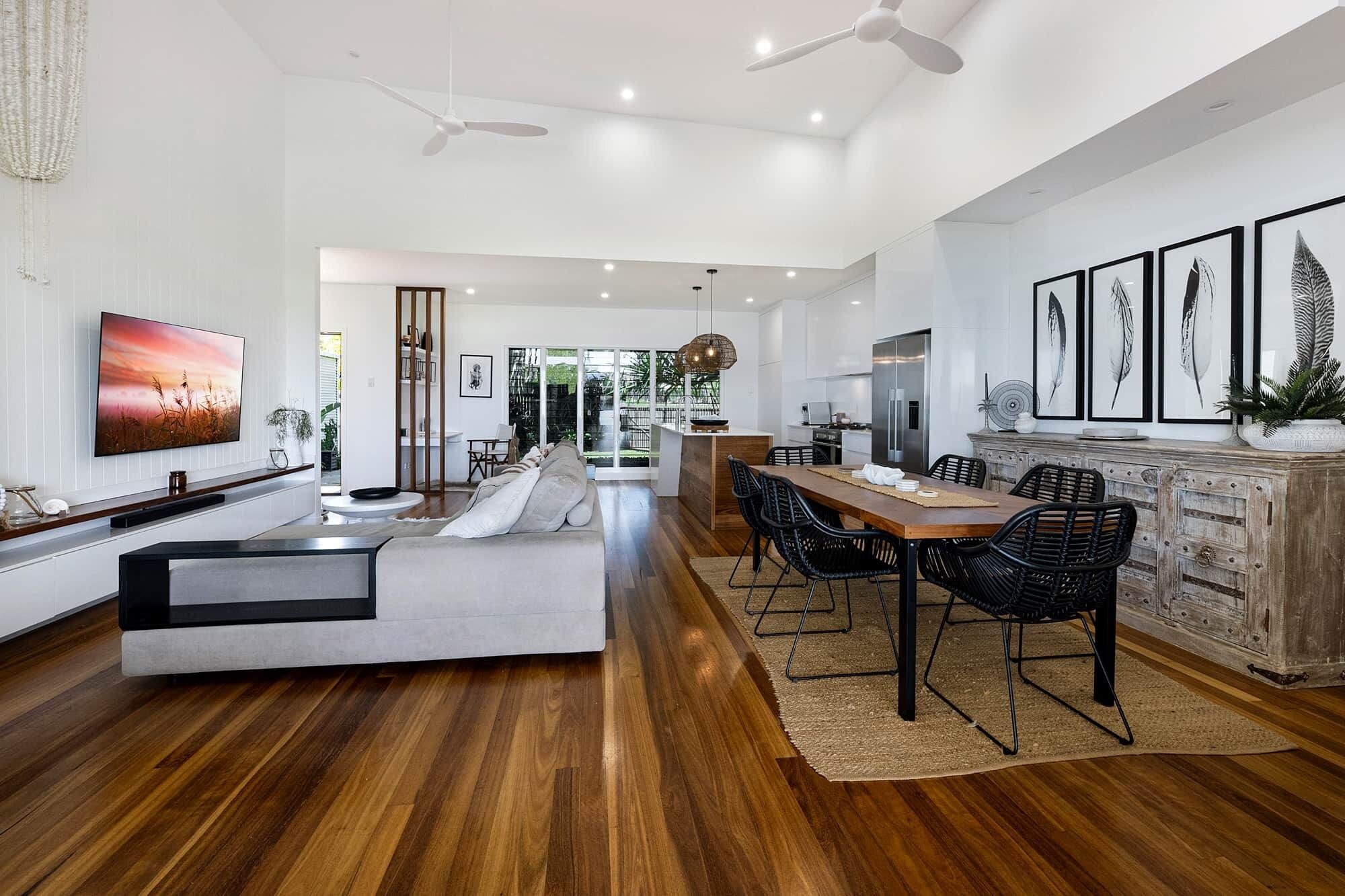 A modern living room with a sofa, dining table, and chairs, a kitchen area, and a large TV on the wall.