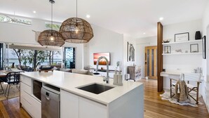 A modern kitchen with a large island, wooden flooring, and pendant lighting.