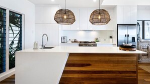 A modern kitchen with a large island, two pendant lights, and a stainless steel refrigerator.