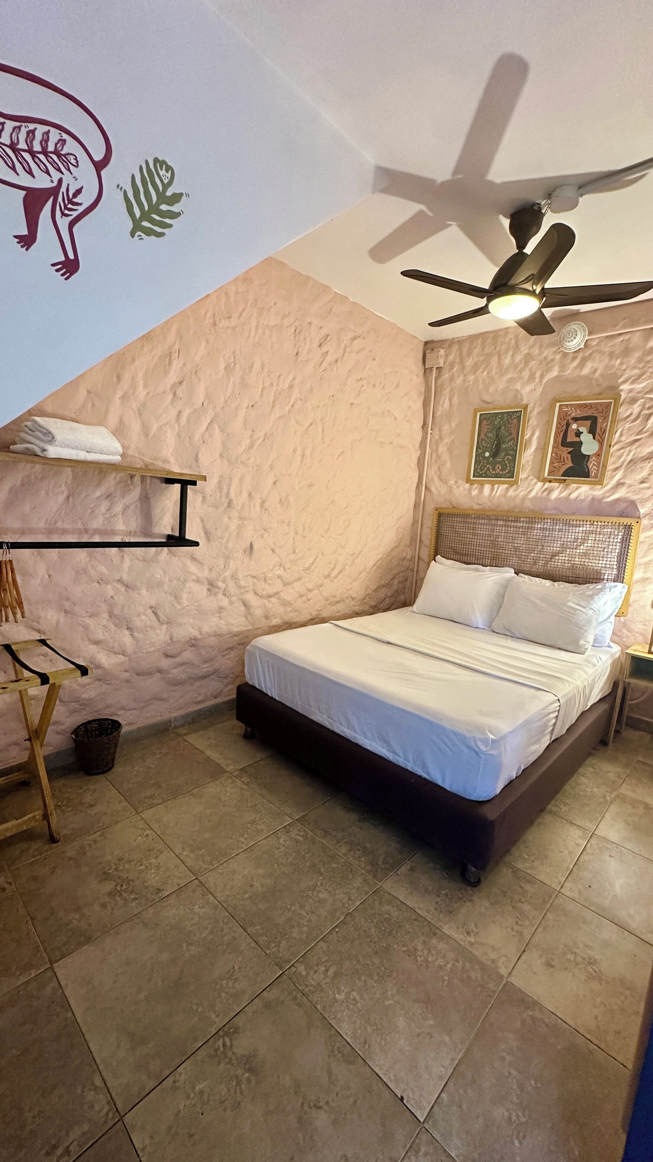 A bedroom with a bed, a ceiling fan, a wall-mounted shelf, and a wall decoration.