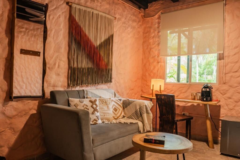 Una habitació acollidora amb un sofà, una taula rodona petita, una làmpada i una finestra amb vistes.