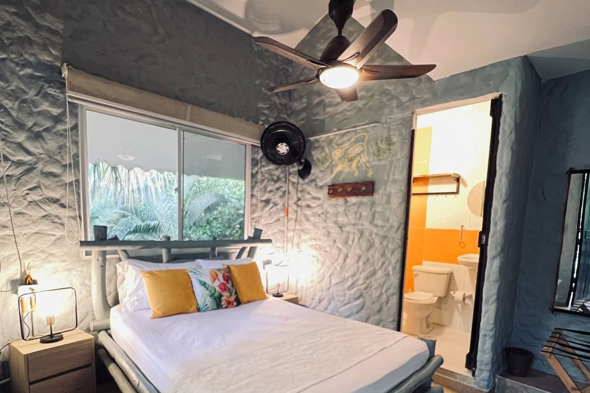 A bedroom with a bed, a nightstand, a window, a ceiling fan, and a view of the outside.