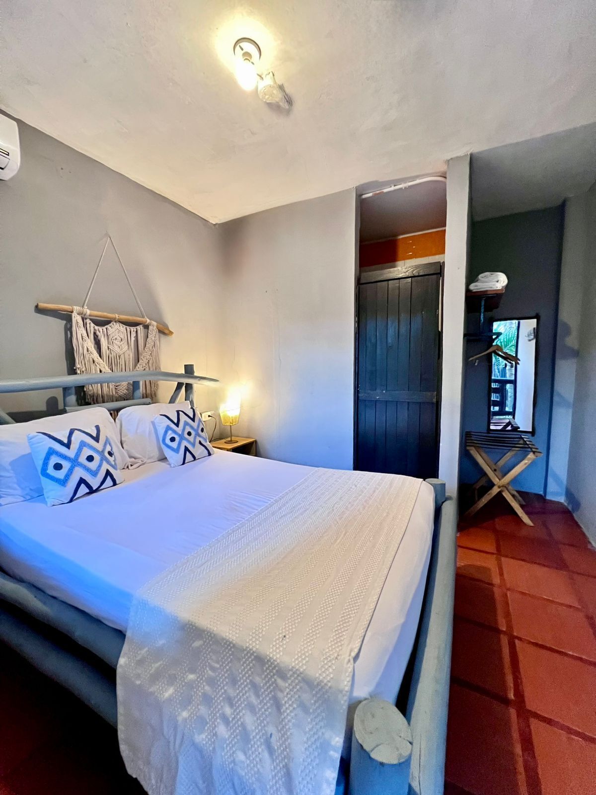A bedroom with a bed, a macrame wall hanging, a nightstand with a lamp, and a wooden door.