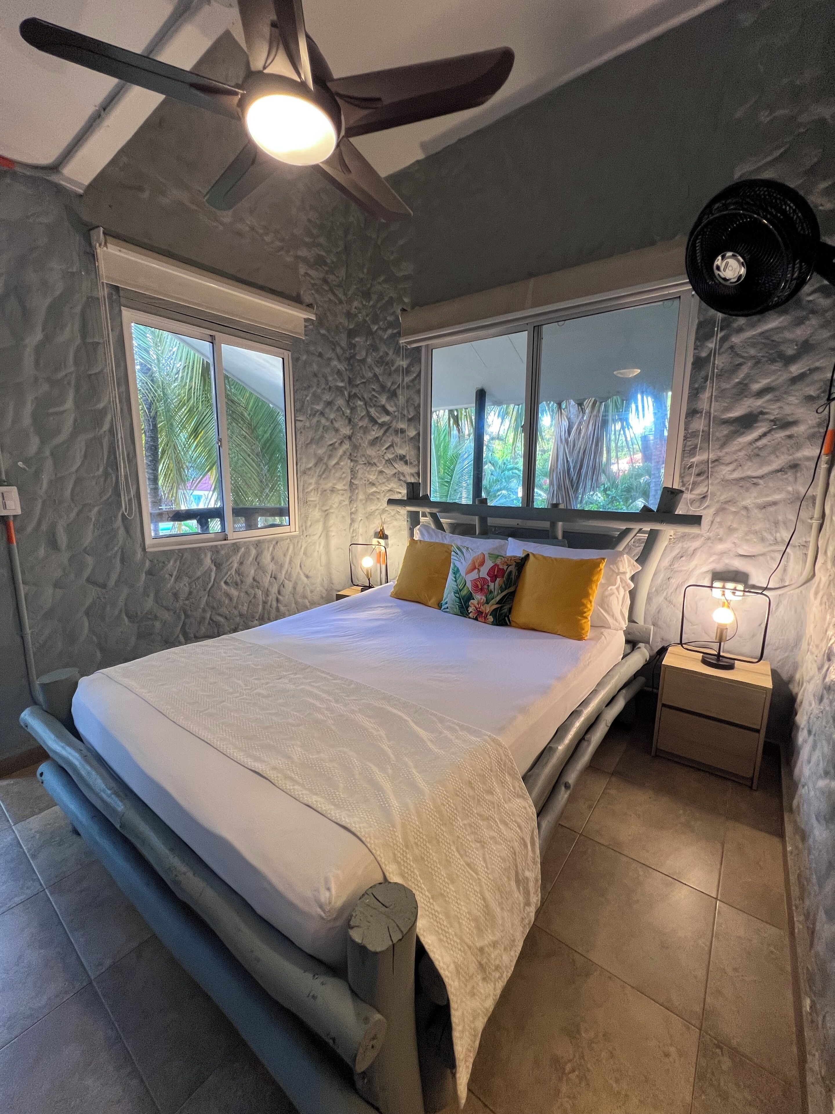 A bedroom with a bed, two bedside tables, a ceiling fan, and windows.