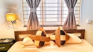 Habitación de hotel con cama, dos almohadas a cuadros, lámpara de noche, mesita de noche con teléfono y ventana con cortinas.