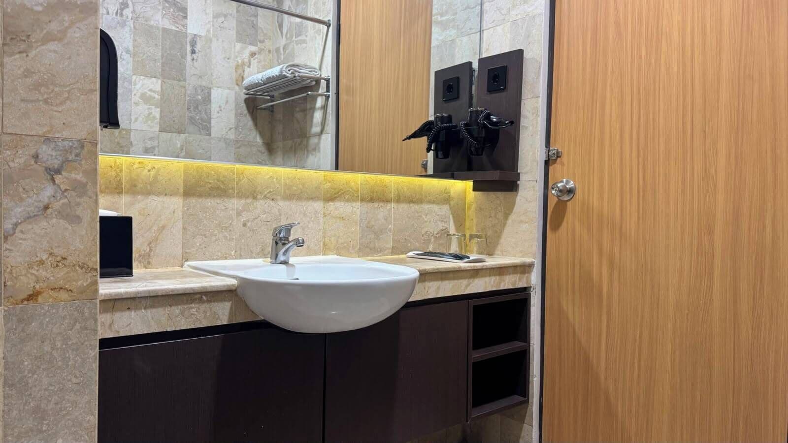 A bathroom with a white sink, dark cabinets, a yellow accent wall, and a wooden door.