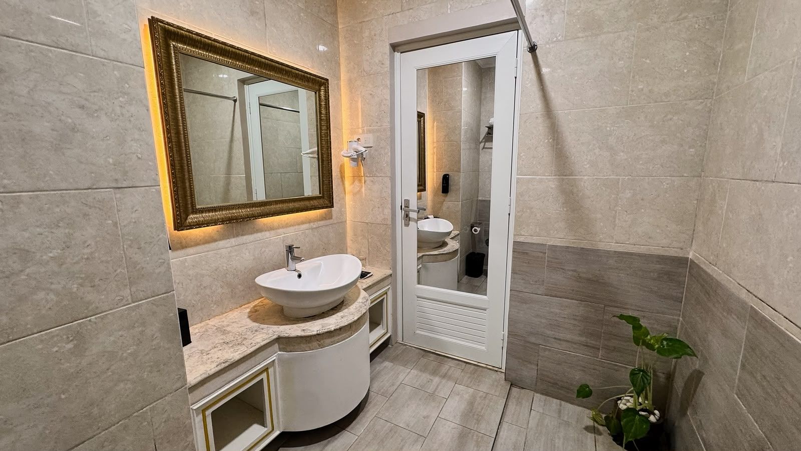 Ein Badezimmer mit einem weißen Waschbecken, einem Spiegel mit goldener Rahmung und einer Duschkabine.