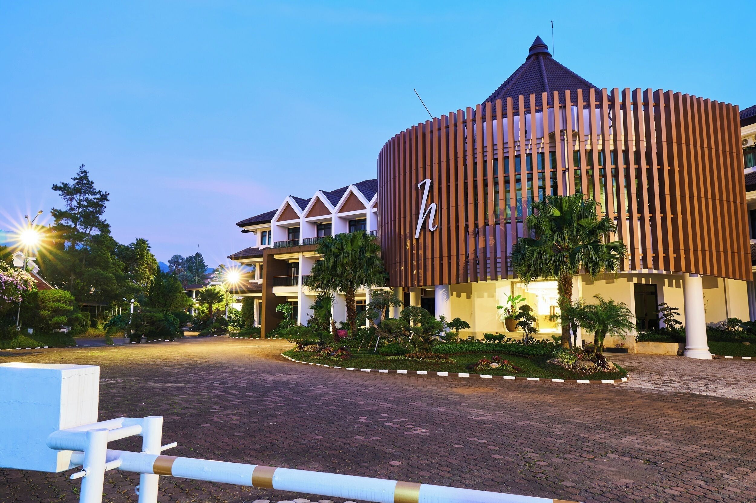 A hotel with a modern design, featuring a prominent 'h' logo, a landscaped entrance, and a paved driveway.