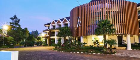 A hotel with a modern design, featuring a prominent 'h' logo, a landscaped entrance, and a paved driveway.