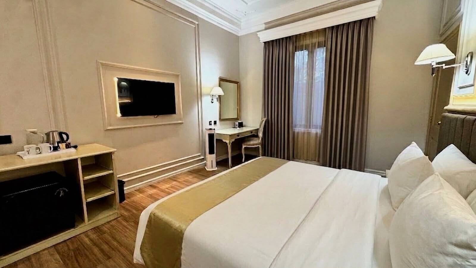 Une chambre d’hôtel avec un lit, un bureau, une télévision et une fenêtre avec des rideaux.