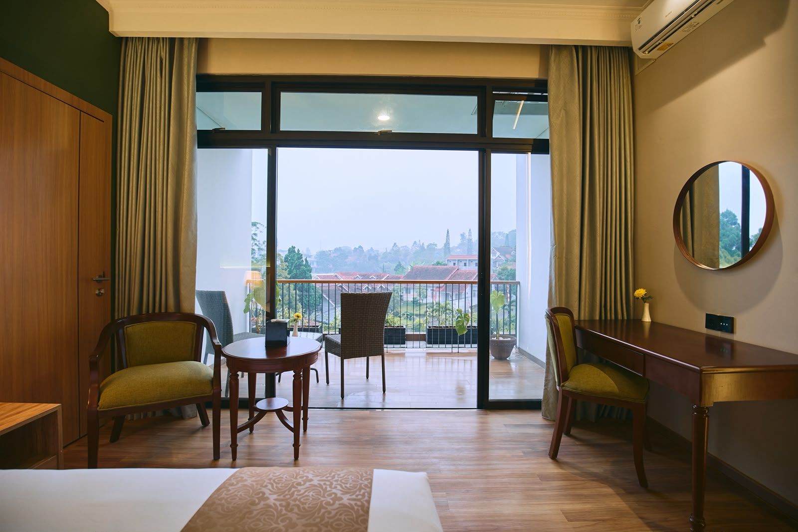 Habitación de hotel con balcón, una mesa redonda, dos sillas, un escritorio y un espejo grande.