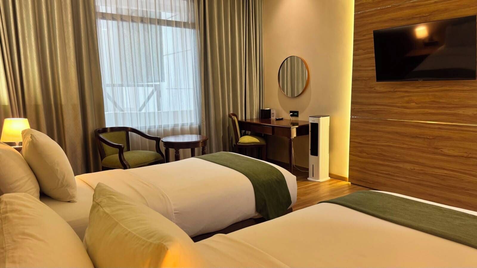 A hotel room with two beds, a desk, a chair, a TV, and a window with curtains.