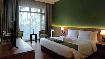 Habitación de hotel con cama, escritorio, dos sillas, una mesita, televisión y ventana con cortinas.
