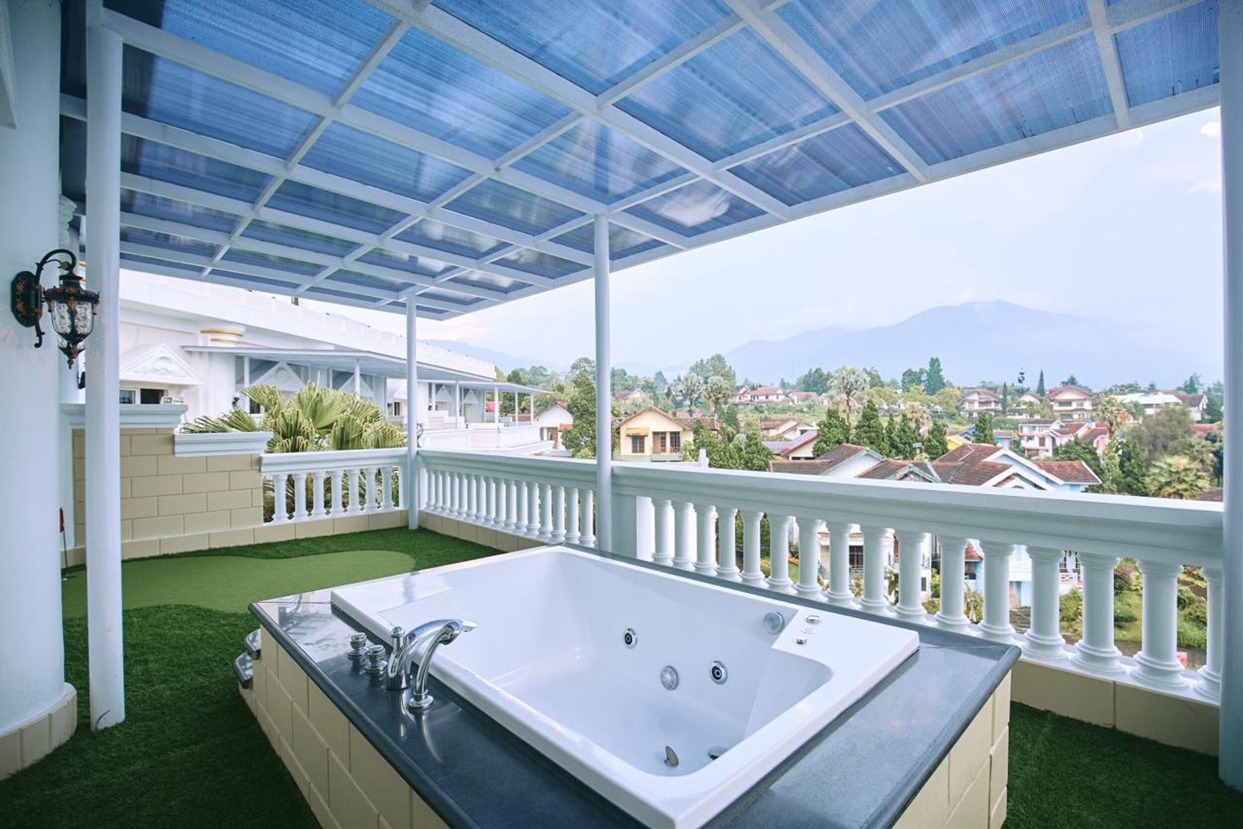 Un balcón con una bañera blanca, vista a casas y una montaña al fondo.