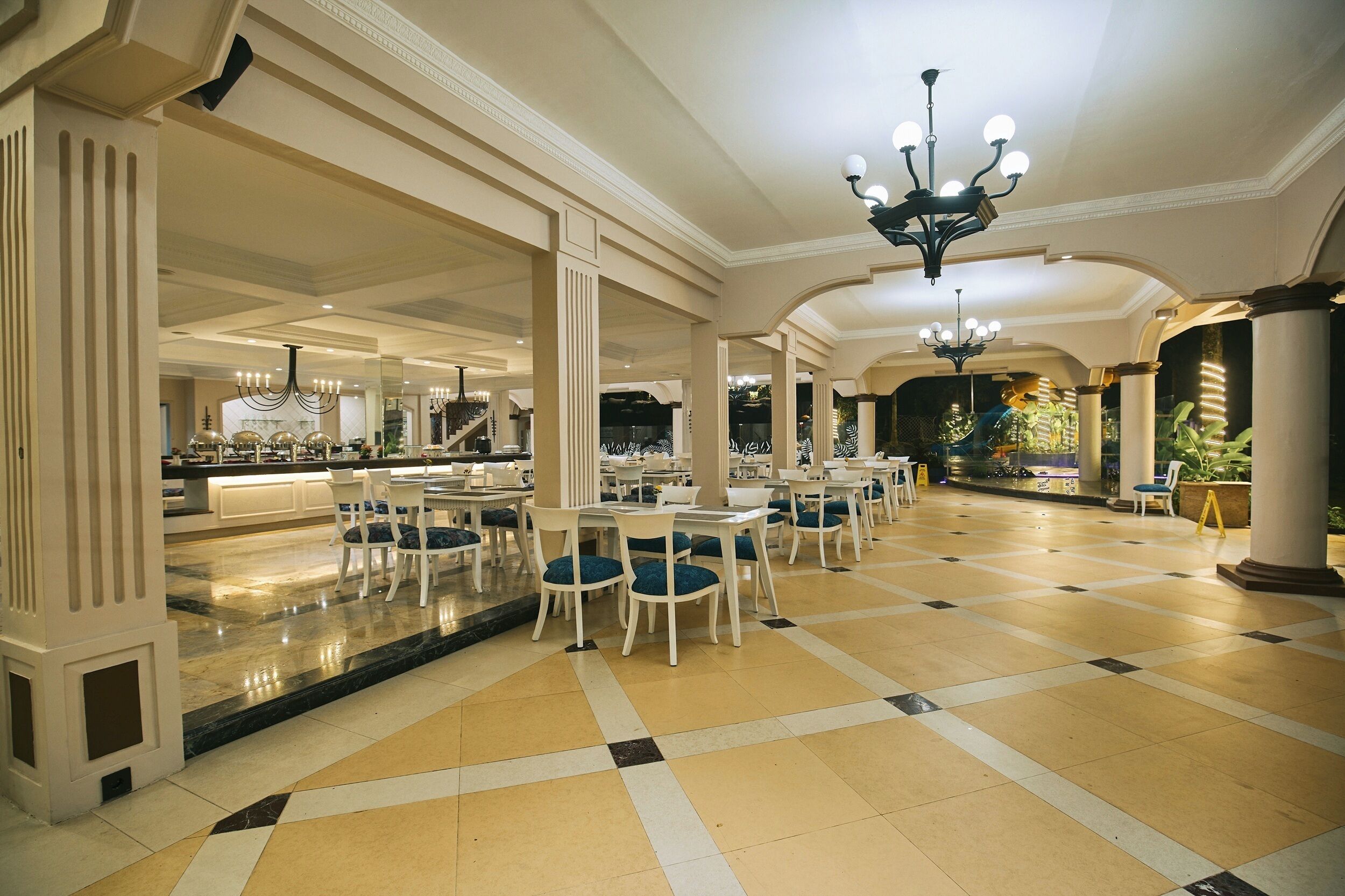 A spacious hotel lobby with a checkered floor, multiple seating areas, and a bar.