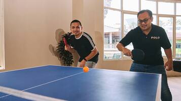 Dos personas jugando ping-pong en una habitación con un ventanal grande y vigas de madera en el techo.