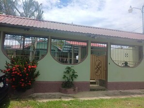 A single-story house with a corrugated metal roof, a front door with a decorative gate, and a large window with a metal grill. - Cieneguita Beach House very close to Cieneguita Beach (Puerto Cortés)