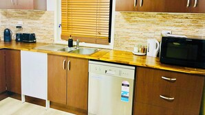A kitchen with wooden cabinets, a dishwasher, a microwave, and a window with blinds.