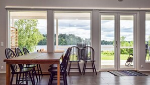 A dining area with a large table and chairs, large windows with a view of a lake and forest, and a sliding glass door leading to an outdoor patio. - Tervaleppä by Interhome (Ikaalinen)