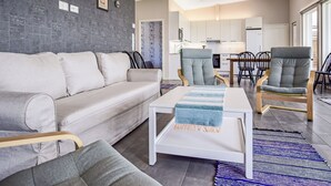 A modern living room with a grey sofa, a matching armchair, and a coffee table. There is a kitchen in the background with white cabinets and a dining area with a wooden table and chairs. - Tervaleppä by Interhome (Ikaalinen)