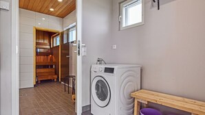 A laundry room with a washing machine, a wooden bench, and two purple buckets. - Tervaleppä by Interhome (Ikaalinen)
