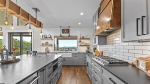 Una cucina moderna con un'isola grande, mobili grigi, dettagli in legno e illuminazione a sospensione.