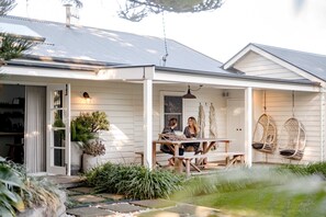 A house with a covered porch, a dining table, and hanging chairs. - Soul of Gerringong Cottage (Gerringong)