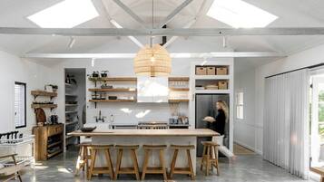 A spacious kitchen with a central island, wooden stools, and a hanging light fixture.