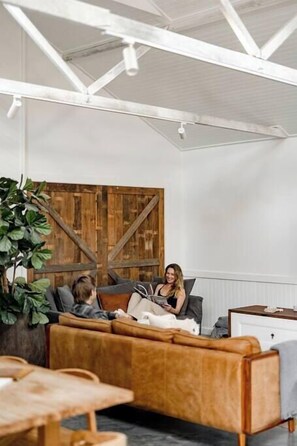 A cozy living room with a large wooden wall, a brown leather sofa, and a dining table. - Soul of Gerringong Cottage (Gerringong)