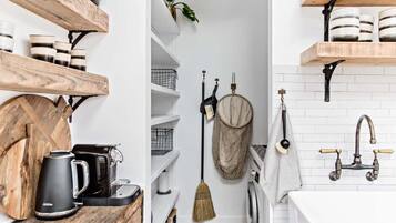 A modern kitchen with wooden shelves, a coffee maker, and a hanging broom.