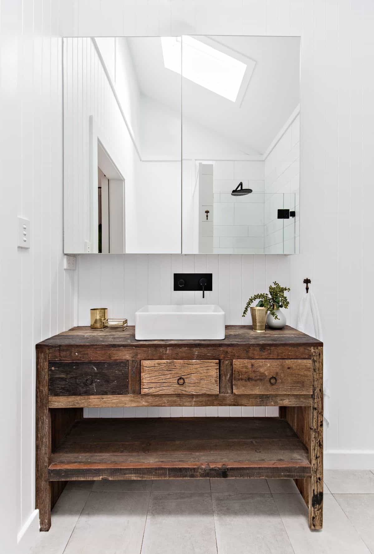 A bathroom with a white vanity, a large mirror, and a shower visible in the reflection.