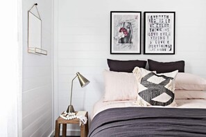 Een slaapkamer met een bed, kussens, een nachtkastje met een lamp en decoratieve wandkunst.
