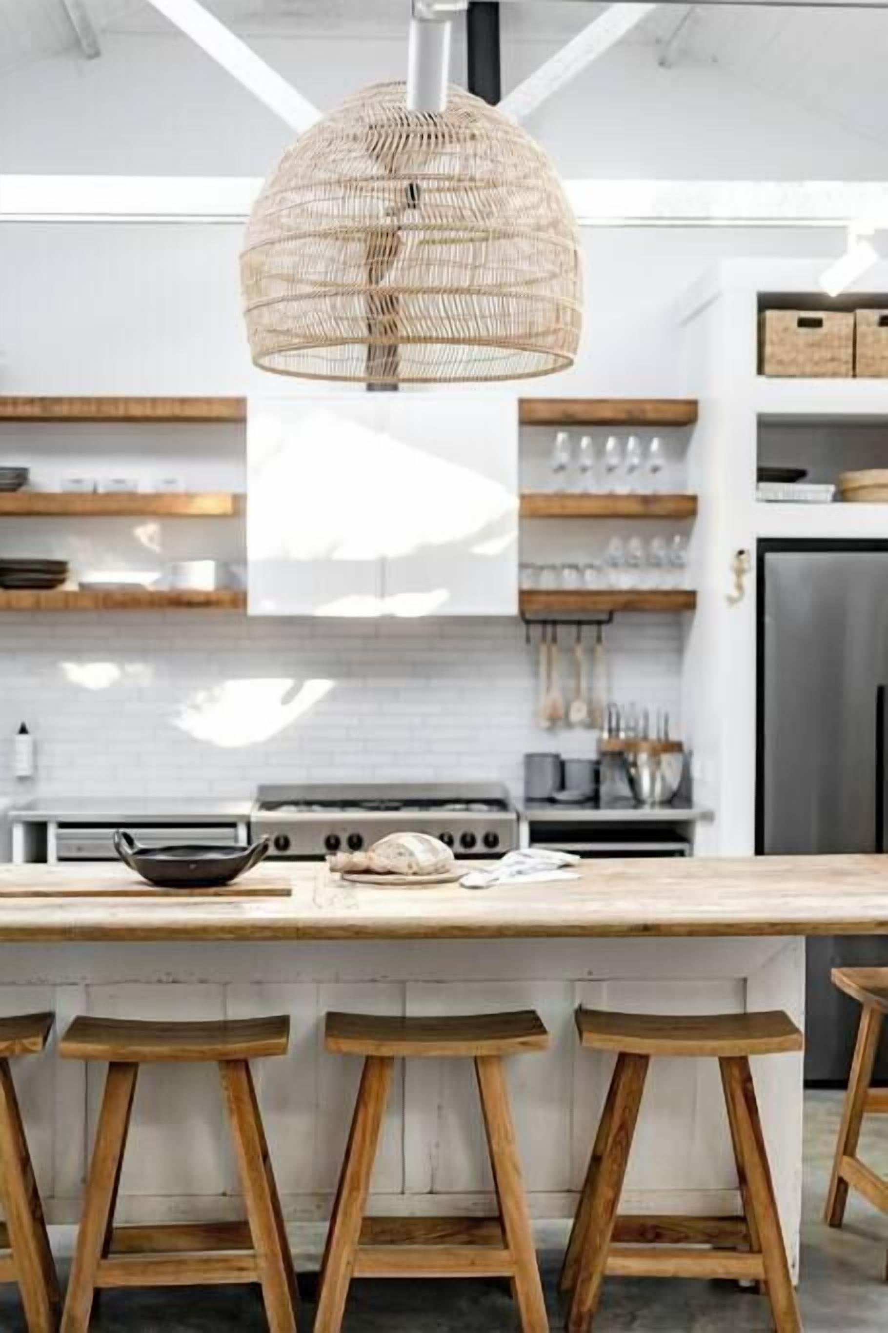 A modern kitchen with a large island, wooden stools, and a woven pendant light.